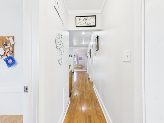 hallway with baseboards, crown molding, and light wood finished floors