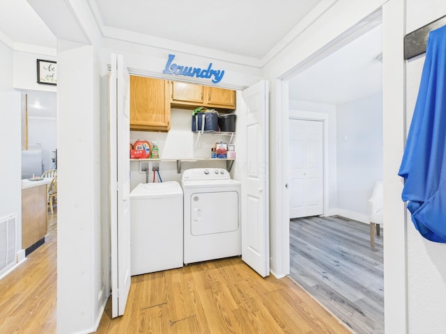 laundry area with light wood-type flooring, cabinet space, ornamental molding, and washer and clothes dryer