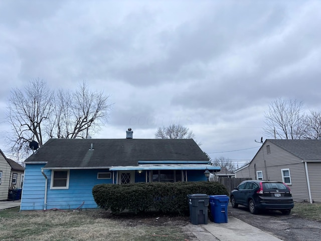 view of front facade with a chimney, a shingled roof, driveway, and fence