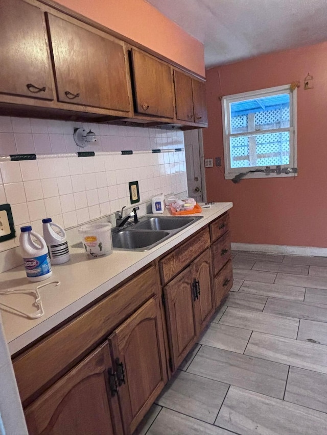 kitchen with baseboards, a sink, light countertops, tasteful backsplash, and brown cabinets