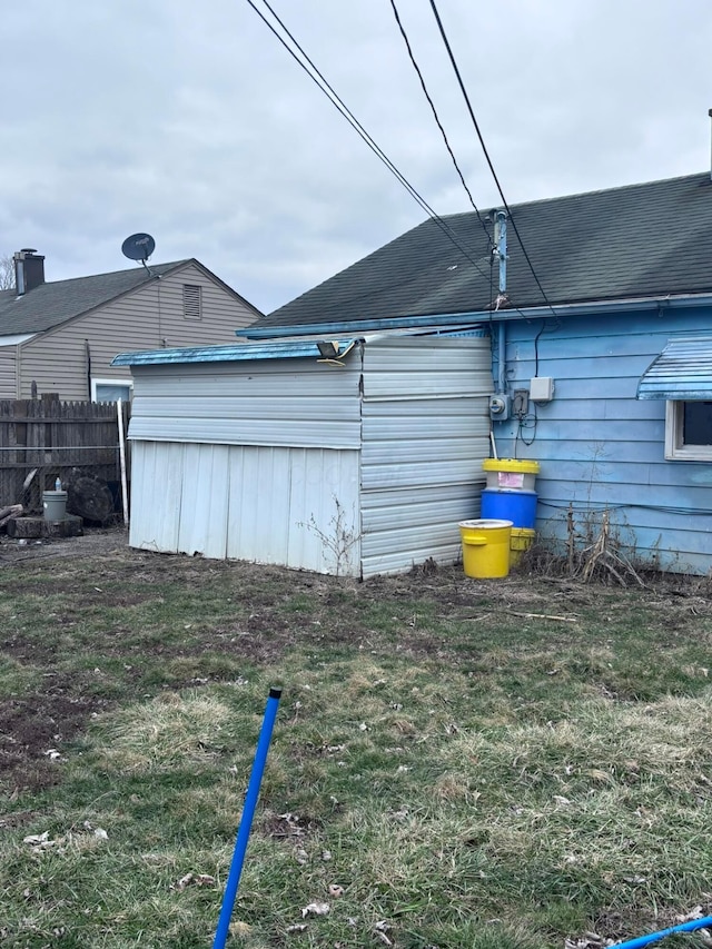 view of side of home with a lawn, a shingled roof, and fence