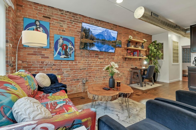 living area featuring visible vents, brick wall, baseboards, and wood finished floors