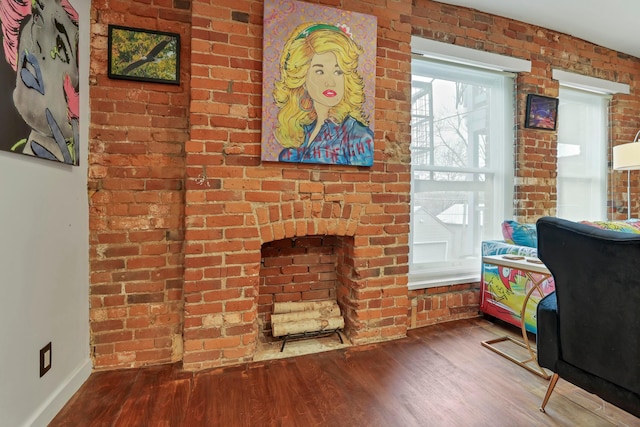 living room featuring wood finished floors, baseboards, and brick wall