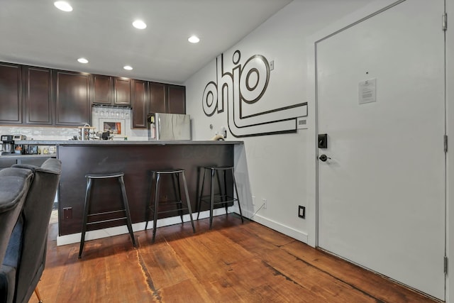 kitchen with backsplash, dark brown cabinets, a kitchen breakfast bar, freestanding refrigerator, and wood finished floors