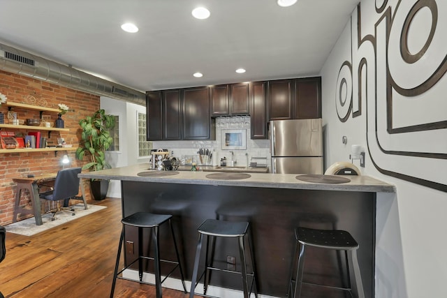 kitchen featuring a kitchen breakfast bar, brick wall, freestanding refrigerator, and wood finished floors