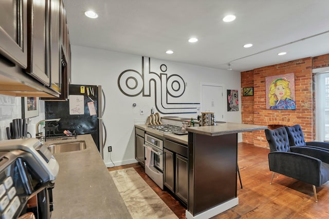 kitchen with brick wall, open floor plan, stainless steel oven, wood finished floors, and a sink