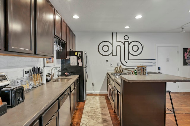 kitchen featuring tasteful backsplash, a sink, a breakfast bar, stainless steel dishwasher, and dark wood-style flooring