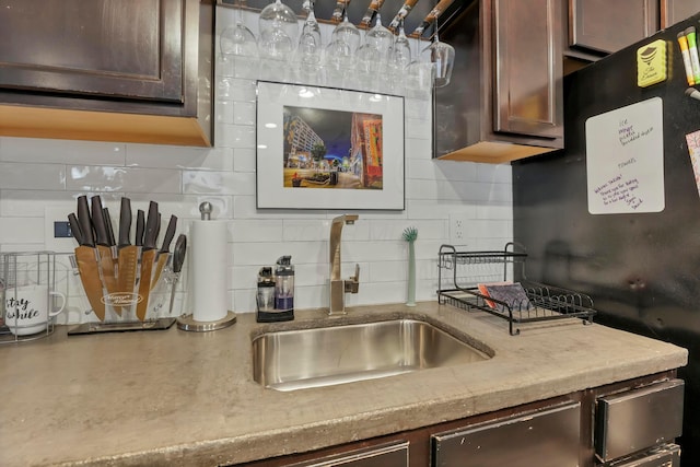 kitchen with a sink, backsplash, dark brown cabinets, and light countertops