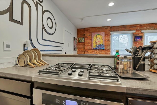 kitchen with oven, brick wall, light countertops, and stainless steel gas cooktop