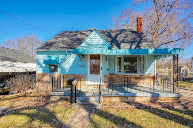 bungalow-style home with roof with shingles, covered porch, and a chimney