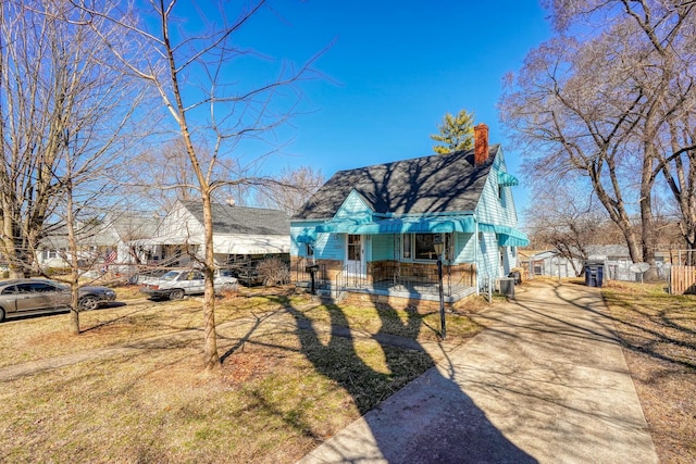 view of front facade with covered porch, a fenced front yard, and a chimney