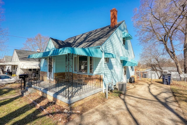 view of front facade featuring a shingled roof, a chimney, central AC, and dirt driveway