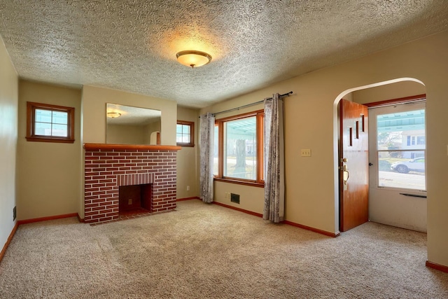 unfurnished living room featuring a wealth of natural light, a brick fireplace, and carpet flooring