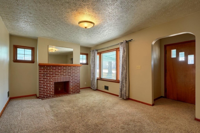 unfurnished living room with arched walkways, plenty of natural light, a brick fireplace, and carpet