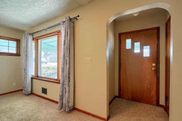 entryway featuring visible vents, baseboards, light colored carpet, arched walkways, and a textured ceiling