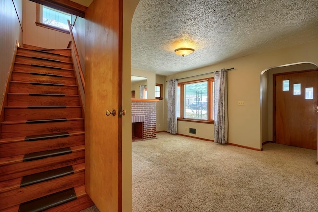 foyer entrance with a brick fireplace, baseboards, carpet flooring, arched walkways, and a textured ceiling