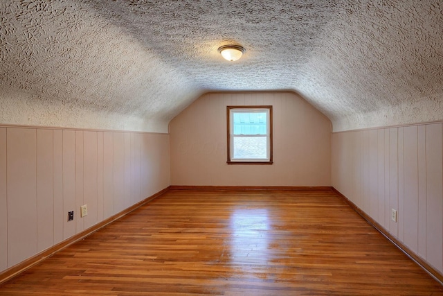 bonus room with lofted ceiling, a textured ceiling, wood finished floors, and wood walls