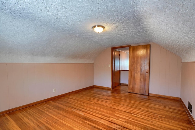 bonus room with lofted ceiling, wood finished floors, baseboards, and a textured ceiling