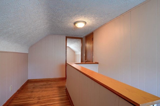 hallway featuring lofted ceiling, wood finished floors, baseboards, and a textured ceiling