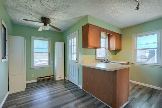 kitchen featuring light countertops, a baseboard heating unit, dark wood-type flooring, and a sink