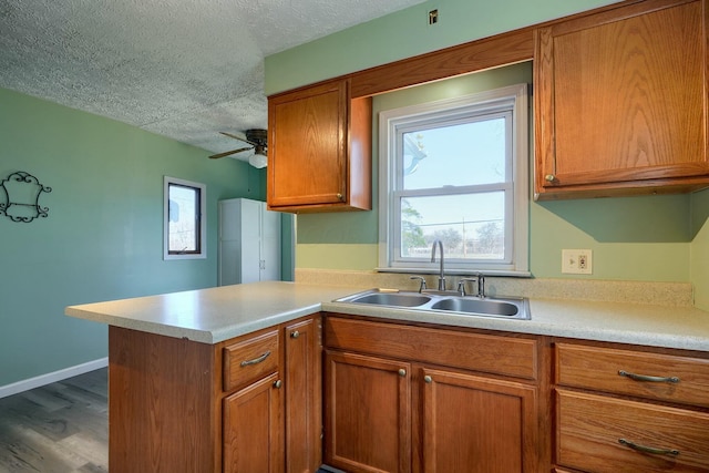 kitchen with a sink, brown cabinets, a textured ceiling, and a peninsula