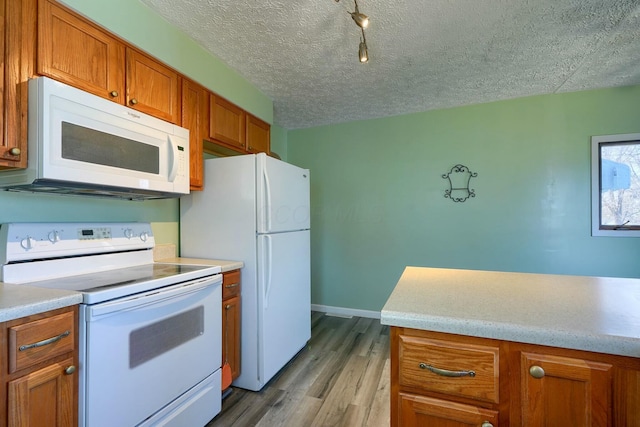 kitchen featuring light wood-type flooring, light countertops, brown cabinets, white appliances, and a textured ceiling