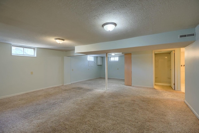 below grade area with a textured ceiling, light colored carpet, visible vents, and baseboards