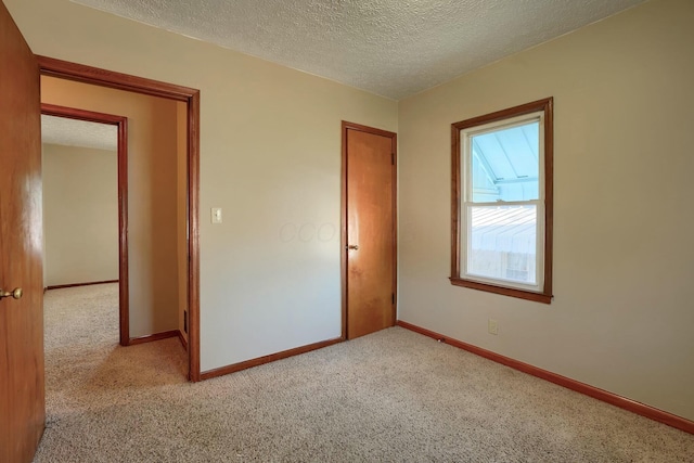 unfurnished bedroom with light colored carpet, baseboards, and a textured ceiling