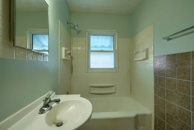 bathroom with a textured ceiling, bathtub / shower combination, and a sink