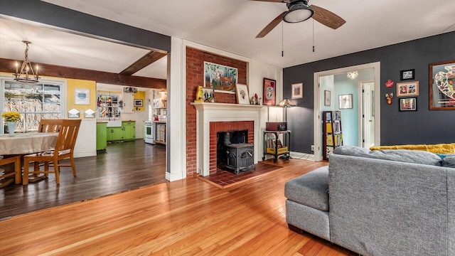 living area with beam ceiling, a wood stove, ceiling fan, and wood finished floors