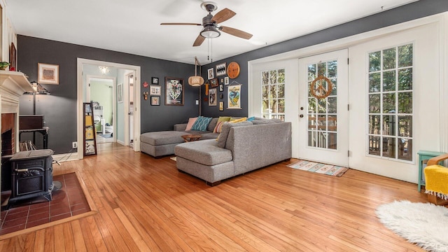 living area with a ceiling fan, baseboards, light wood finished floors, a wood stove, and french doors