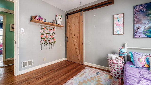 living area with a barn door, wood finished floors, visible vents, and baseboards