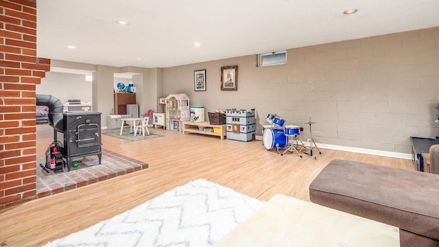 rec room with recessed lighting, a wood stove, concrete block wall, and wood finished floors