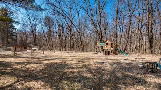 view of yard with an outdoor structure, a wooded view, and a playground