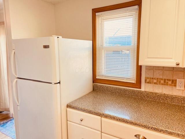 kitchen featuring backsplash, white cabinets, freestanding refrigerator, and light stone countertops