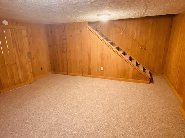 finished below grade area featuring wooden walls, carpet flooring, a textured ceiling, and stairs