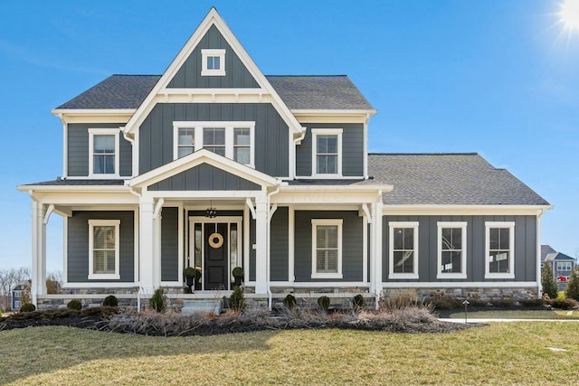 view of front of home with covered porch, board and batten siding, a shingled roof, and a front yard