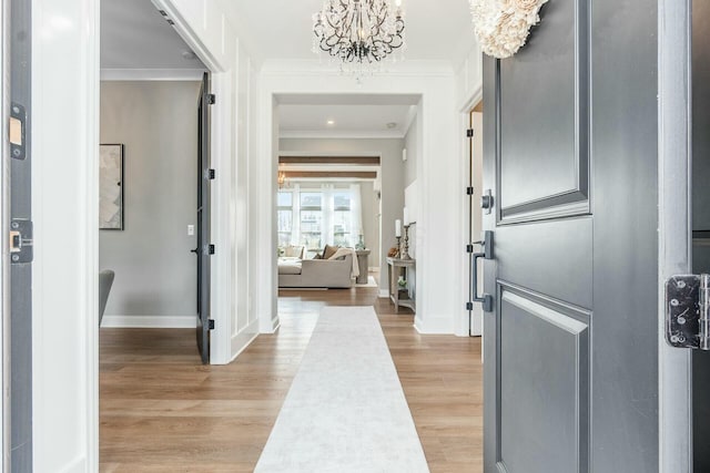 entrance foyer featuring a notable chandelier, baseboards, crown molding, and light wood-style floors