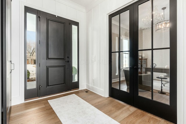 foyer entrance with visible vents, wood finished floors, ornamental molding, and a decorative wall