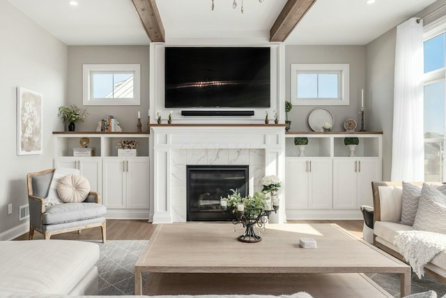 living room featuring beam ceiling, wood finished floors, and a fireplace