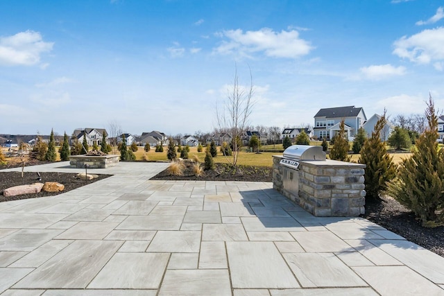 view of patio / terrace featuring a residential view, a fire pit, a grill, and exterior kitchen