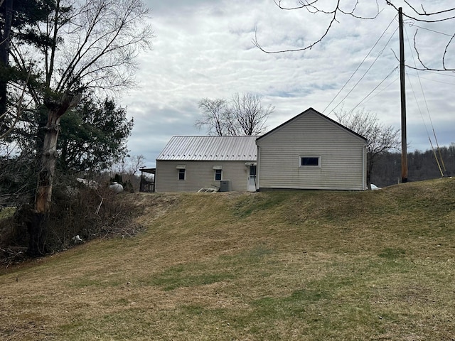 rear view of property featuring central air condition unit, a lawn, and metal roof