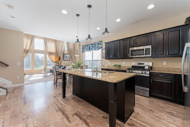 kitchen with light stone counters, stainless steel appliances, light wood-type flooring, and a sink