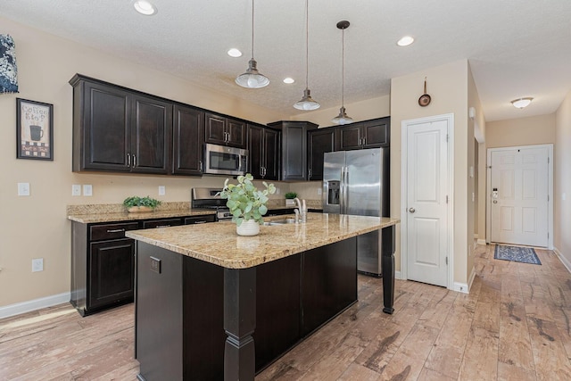 kitchen featuring hanging light fixtures, stainless steel appliances, light wood-type flooring, and light stone counters