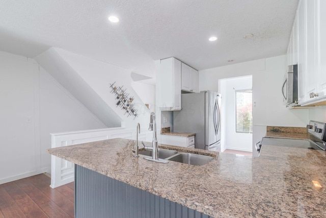 kitchen with a sink, a textured ceiling, dark wood finished floors, appliances with stainless steel finishes, and white cabinets