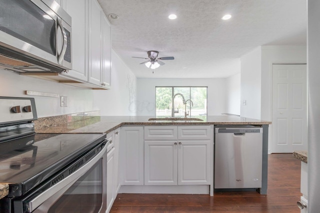 kitchen with light stone counters, a peninsula, a sink, dark wood-type flooring, and appliances with stainless steel finishes