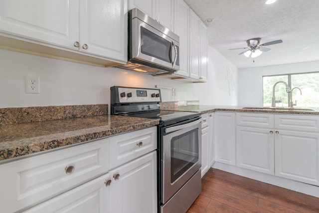 kitchen with a sink, dark stone countertops, dark wood-style floors, white cabinetry, and stainless steel appliances