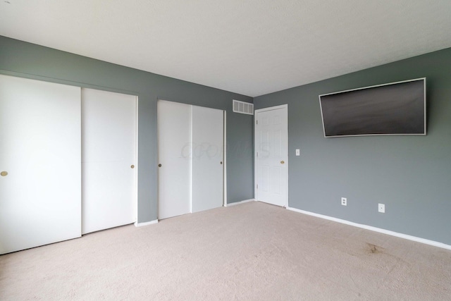 unfurnished bedroom with visible vents, multiple closets, baseboards, and carpet flooring