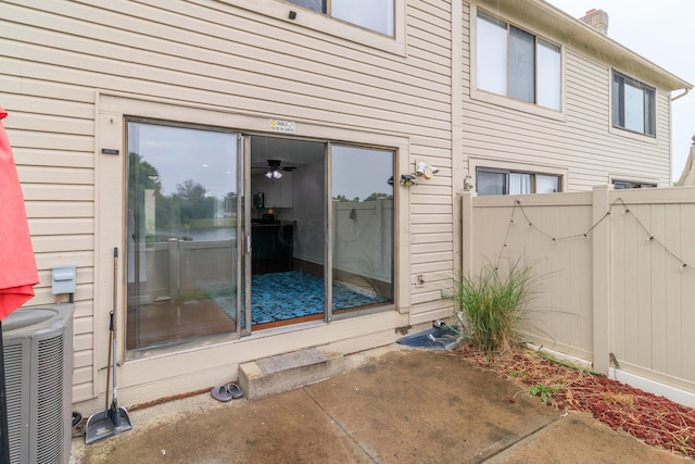 view of exterior entry featuring a patio, fence, central AC, and a gate