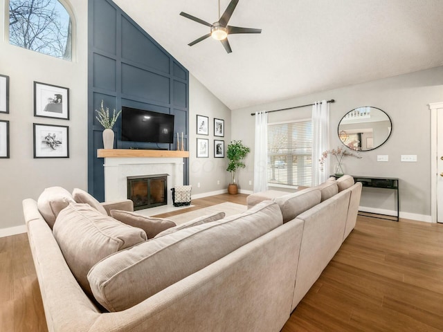 living area featuring high vaulted ceiling, a ceiling fan, wood finished floors, a large fireplace, and baseboards